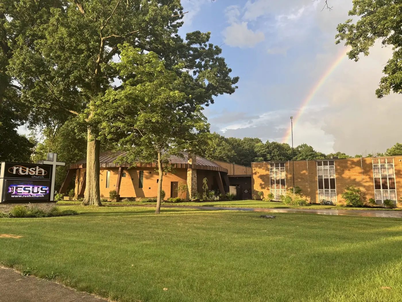 The Rush Church building and lawn sign under a rainbow on Glenwood Ave